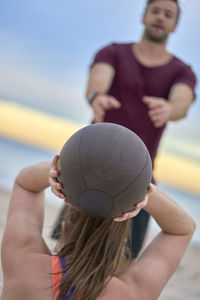 Fitness instructor assisting woman in exercising at beach