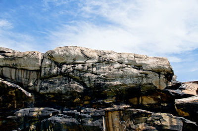 Low angle view of rock formations against cloudy sky during sunny day