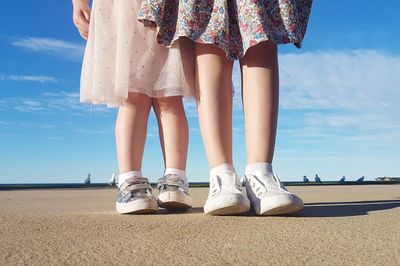 Low section of girls standing at beach on sunny day