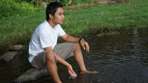 Side view of teenage boy sitting by lake