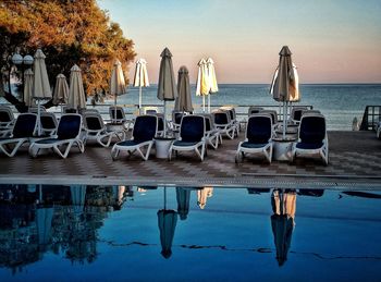 Deck chairs by swimming pool against sky