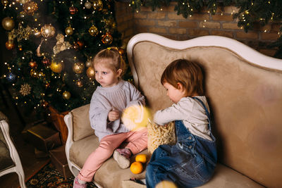 Little children ride toy horses in decorated christmas interior.