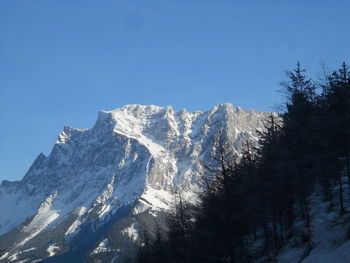 Low angle view of snowcapped mountains against clear blue sky