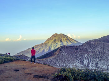 Rear view of man standing on mountain against sky