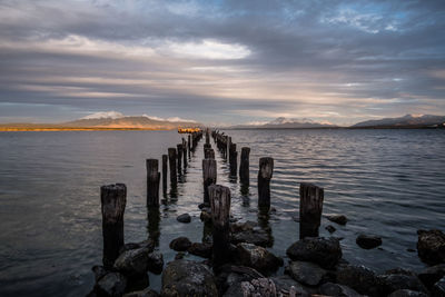 Wooden posts in sea during sunset