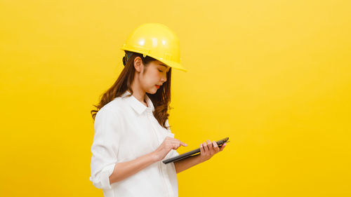 Young woman using mobile phone against yellow background