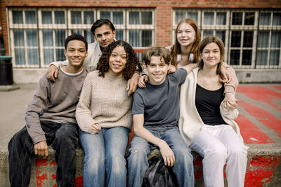 Smiling male and female teenage students sitting together in high school campus