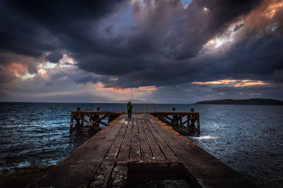 Pier by sea against cloudy sky during sunset