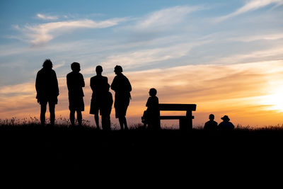 Silhouette people standing on field against sky during sunset