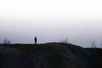 Rear view of man walking on mountain against clear sky