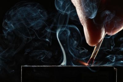 Cropped hand igniting matchstick against black background