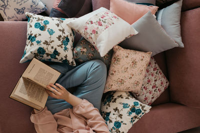 Directly above shot of woman reading book sitting on sofa at home