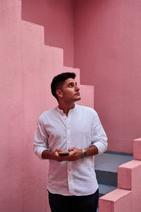 Young latin man holds his cell phone in a pink building