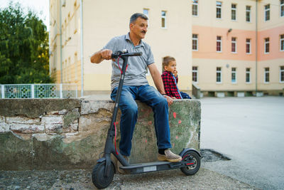 Father and son with push scooter sitting on retaining wall