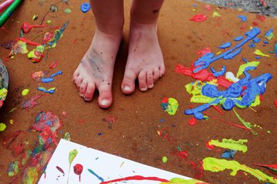 Low section of child standing on surface with messy paint