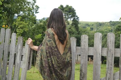 Woman standing by fence against trees