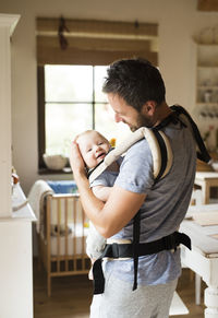 Happy father with baby in baby carrier at home