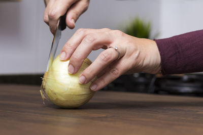 Cropped hands of woman cutting onion on wooden table