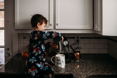 Young boy sitting on counter making coffee for dad