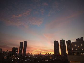 Illuminated buildings in city against sky during sunset