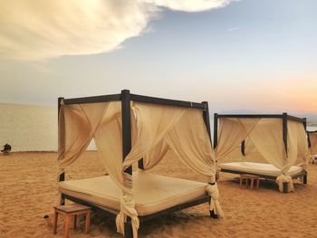 Chairs on beach against sky during sunset