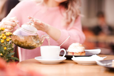 Midsection of teenager pouring tea in cup at restaurant