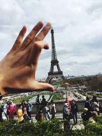 Optical illusion of hand holding eiffel tower against cloudy sky