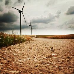 Road passing through field against cloudy sky