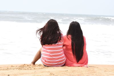 Rear view of friends looking at sea while sitting on shore