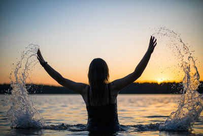 Girl in a long black swimsuit swims outside the city on the lake in the rays of sunset or dawn.