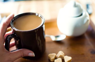 Close-up of hand holding coffee cup on table