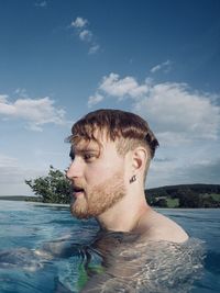 Portrait of shirtless young man in swimming pool against sky