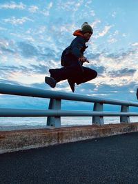 Side view of man on railing against sky