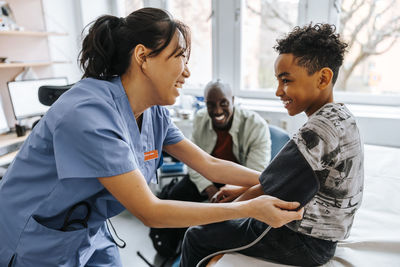 Happy female pediatrician checking boy's blood pressure in examination room