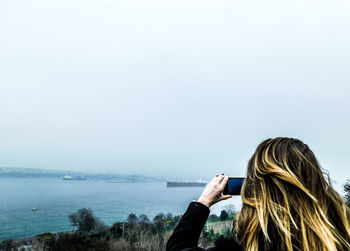 Rear view of woman photographing sea against clear sky