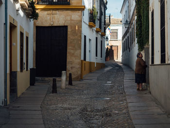 Rear view of man walking on footpath amidst buildings