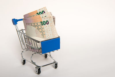 Close-up of paper currency in shopping cart against white background