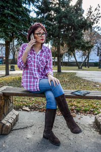 Full length of young woman talking on phone while sitting on bench at park