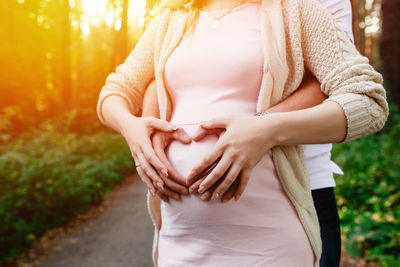 Midsection of man with pregnant wife making heart shape on belly