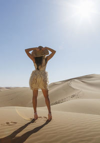 Full length of woman standing on sand at beach against clear sky