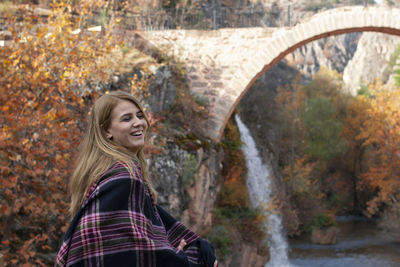 Portrait of young woman standing against waterfall