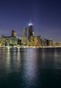 Illuminated cityscape by sea against sky at night