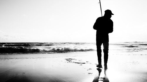 Silhouette man fishing at beach against sky