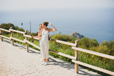 Woman standing on railing by sea against sky