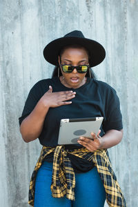 Young woman using mobile phone while standing against wall