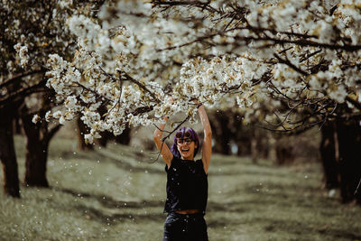 Full length of woman standing by cherry blossom tree