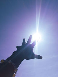 Low angle view of sunlight streaming through hand against sky