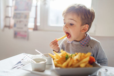 Cute boy eating food at table