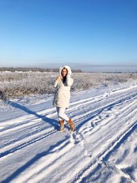 Full length of woman standing on snow against blue sky