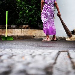 Low section of woman holding broom while standing footpath